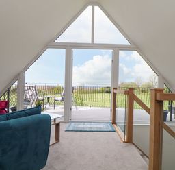 A sitting area with a blue sofa and glass door leading to a balcony with chairs at Higher Kernick View in Helland near Blisland