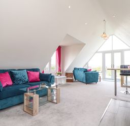 An attic living room with blue sofas pink cushions glass coffee table and a dining area with stools at Higher Kernick View in Helland near Blisland