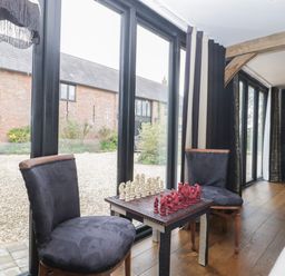 A small table with a chess set between two chairs near large glass doors in a room with wooden floors at The Courtyard - Hilltop Barn in Winterborne Zelston near Wareham
