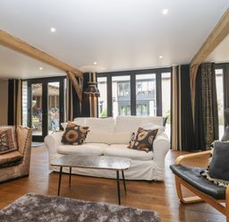 A living room with a white sofa, armchairs, a coffee table, wooden beams, and large windows at The Courtyard - Hilltop Barn in Winterborne Zelston near Wareham