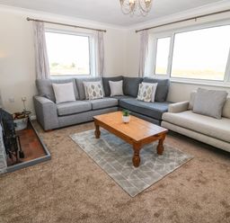A living room with two sofas a wooden coffee table and a fireplace at Windy Ridge in Trearddur Bay