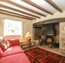 A living room with wooden ceiling beams a stone fireplace a red sofa and a lamp on a wooden bench at Field View in Curland near Taunton