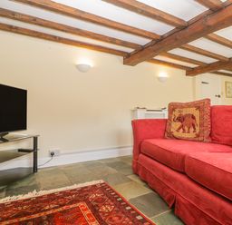 A living room with a red sofa a patterned cushion a television on a black glass stand and wooden ceiling beams at Field View in Curland near Taunton