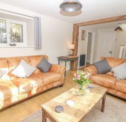 A living room with two brown leather sofas a wooden coffee table with flowers a small desk lamp and a staircase at Pumphouse Cottage in Uffculme