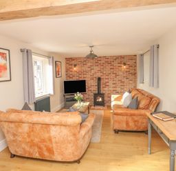 A living room with two brown sofas a wooden coffee table and a wood stove against a brick wall at Pumphouse Cottage in Uffculme