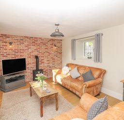 A living room with leather sofas a wooden coffee table and a television on a stand at Pumphouse Cottage in Uffculme