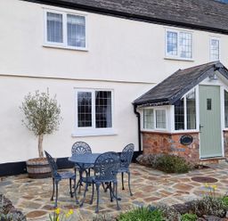 A patio with a metal table and four chairs outside a cottage with white walls and a green door at Pumphouse Cottage in Uffculme