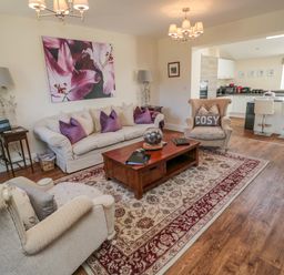A living room with beige sofas purple cushions a wooden coffee table and lamps at Cushat House Stamford near Embleton
