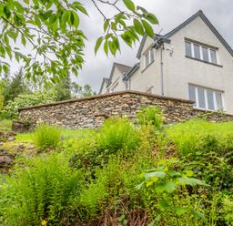 A stone house seen from a garden with stone steps and green plants at Hazelseat House in Graythwaite near Ulverston