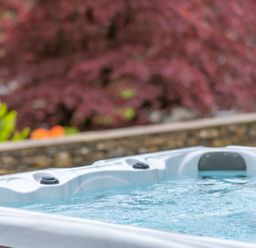 A hot tub with water and headrests near a stone wall and trees at Hazelseat House Graythwaite near Ulverston