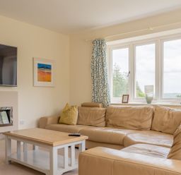 A living room with a leather sofa a wooden coffee table a wall-mounted tv and a window with curtains at Hazelseat House in Graythwaite near Ulverston