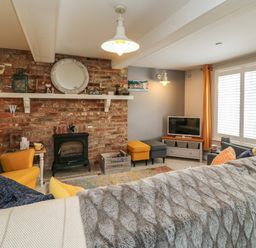 A living room with a brick fireplace yellow armchairs a television and a window with orange curtains at Harbour Reach Brewers Quay Harbour