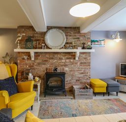 A living room with a yellow armchair a brick fireplace and a television at Harbour Reach Brewers Quay Harbour