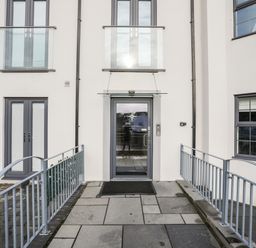 The entrance door of a modern apartment building with railings on both sides of the pathway at Steps Away Benllech