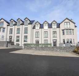 A large white residential building with multiple windows and balconies and a paved parking area in front at Steps Away in Benllech