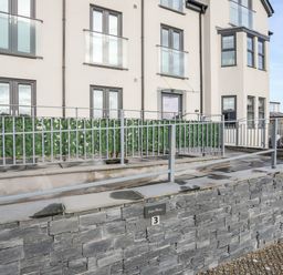 A building with grey framed windows and railings with a stone wall and a sign displaying number 3 at Steps Away in Benllech