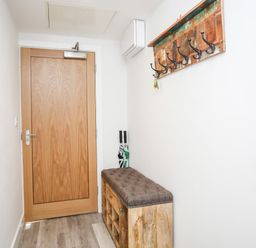 A hallway with a wooden door a wooden bench with cushions and a wall-mounted coat rack at Steps Away in Benllech