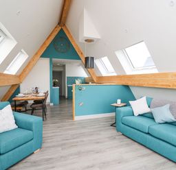 An attic living area with turquoise sofas dining table and kitchen at Kerry Hill - The Sheepfold in Llanyre near Llandrindod Wells