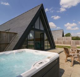A patio with a hot tub and wooden chairs with a table outside a triangular roof building at Kerry Hill - The Sheepfold in Llanyre near Llandrindod Wells