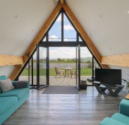 A living room with teal sofas a television and a glass door opening to a patio with chairs at Kerry Hill - The Sheepfold in Llanyre near Llandrindod Wells