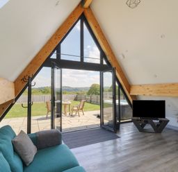 A living room with a teal couch a TV on a stand a potted plant and open glass doors leading to a patio and garden at Kerry Hill - The Sheepfold in Llanyre near Llandrindod Wells