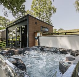 A hot tub next to a house with a view of trees at The Fox Den Nantmel near Rhayader