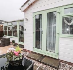 An outdoor patio area with green framed glass doors and windows with a wicker sofa and a flower pot on a wicker table at Swale Cottage in Beadnell