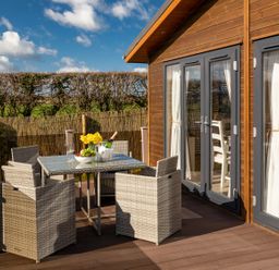 An outdoor patio with a glass table and four wicker chairs next to a house with glass doors at Lobster Lodge in Runswick Bay