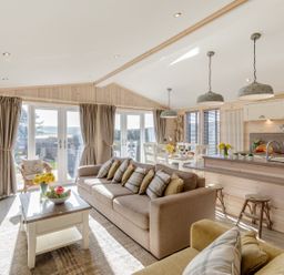 An open living area with sofas coffee table kitchen island dining table and large windows at Lobster Lodge in Runswick Bay