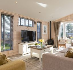 A living room with a TV on a stand a coffee table with fruit and flowers and sofas at Lobster Lodge in Runswick Bay