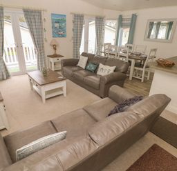 A living room with two leather sofas a coffee table a dining table and kitchen counter at Cwtch Lodge 42 Stepaside near Wisemans Bridge