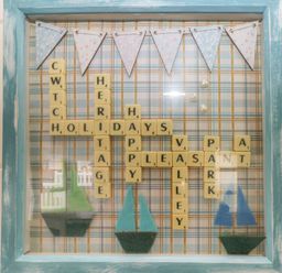 A framed decorative board with Scrabble tiles spelling words and paper sailboats at Cwtch Lodge 42 Stepaside near Wisemans Bridge