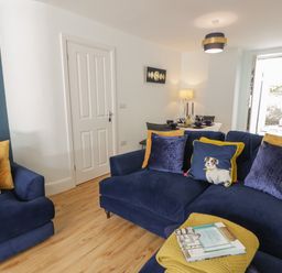 A living room with blue sofas and yellow cushions next to a dining table set at Bryn Derfel in Borth-y-Gest near Porthmadog