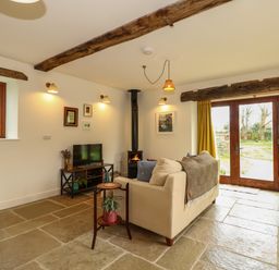 A living room with a fireplace television sofa and wooden beams at The Little Hay Barn in Bacton