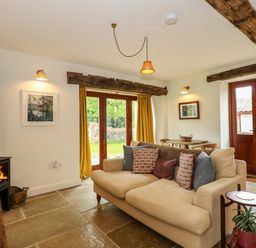A living room with a beige sofa cushions wood burning stove and wooden doors at The Little Hay Barn in Bacton