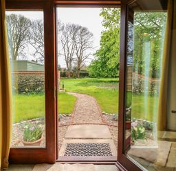 A doorway with glass doors opening to a garden with a gravel path and grassy area at The Little Hay Barn in Bacton