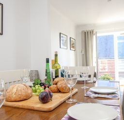 A dining table set with plates glasses and bread in a room with framed pictures and a large window at Castle Cove View in Castle Cove