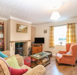 A living room with armchairs a coffee table a wood burning stove and a bookshelf at Rose Cottage in Downham Market