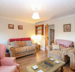 A sitting room with upholstered chairs a glass coffee table wooden floor and framed pictures on the walls at Rose Cottage in Downham Market
