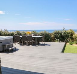 A wooden deck patio with a dining table and chairs a hot tub and ocean view at Pepperpots in Mawgan Porth
