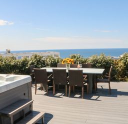 An outdoor dining table with chairs and a vase of sunflowers next to a hot tub on a deck with ocean view at Pepperpots in Mawgan Porth