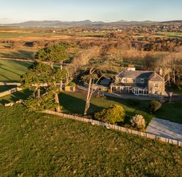A stone house surrounded by trees and fenced grassy fields in a rural area at Bennar Fawr in Dyffryn Ardudwy