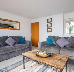 A living room with two gray sofas with blue and gray cushions a wooden coffee table with decorative items and a rug at Awel Y Mor in Criccieth