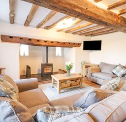 A living room with exposed wooden beams a wood stove two sofas a coffee table with flowers and a wall-mounted television at Plas Iolyn in Pentrefoelas near Betws-Y-Coed