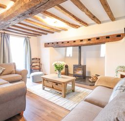 A living room with wooden ceiling beams sofas a coffee table with flowers and a wood-burning stove at Plas Iolyn in Pentrefoelas near Betws-Y-Coed