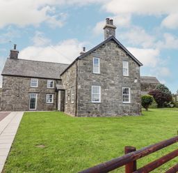 A stone house with white framed windows on green lawn near wooden fence at Plas Iolyn in Pentrefoelas near Betws-Y-Coed