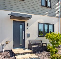 The exterior entrance of a modern house with a dark door bench and small bushes at Sea View in Llanfaelog