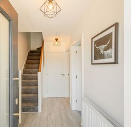 A hallway with carpeted stairs a closed white door light fixtures and wall art at Sea View in Llanfaelog