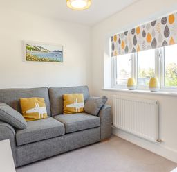 A small living room with a gray sofa with yellow cushions by a window with patterned blinds at Sea View in Llanfaelog