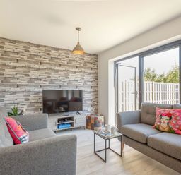 A living room with two grey sofas a television on a stand and glass doors opening to a fenced garden at Sea View in Llanfaelog